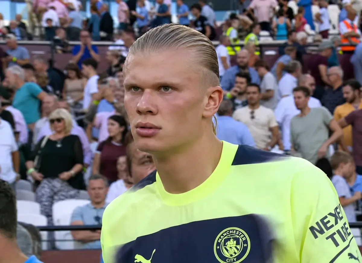 Erling Haaland in Manchester City kit, with the Etihad Stadium in the background.